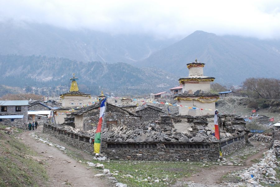 Traditional stone stupas with prayer flags in Himalayan village, mountains in background